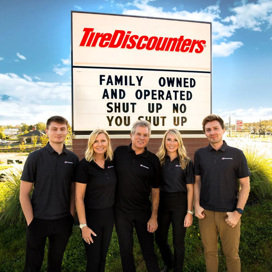 Tire Discounters family members, standing in front of store sign reading “Family Owned and Operated,” highlighting the brand’s family-run values.