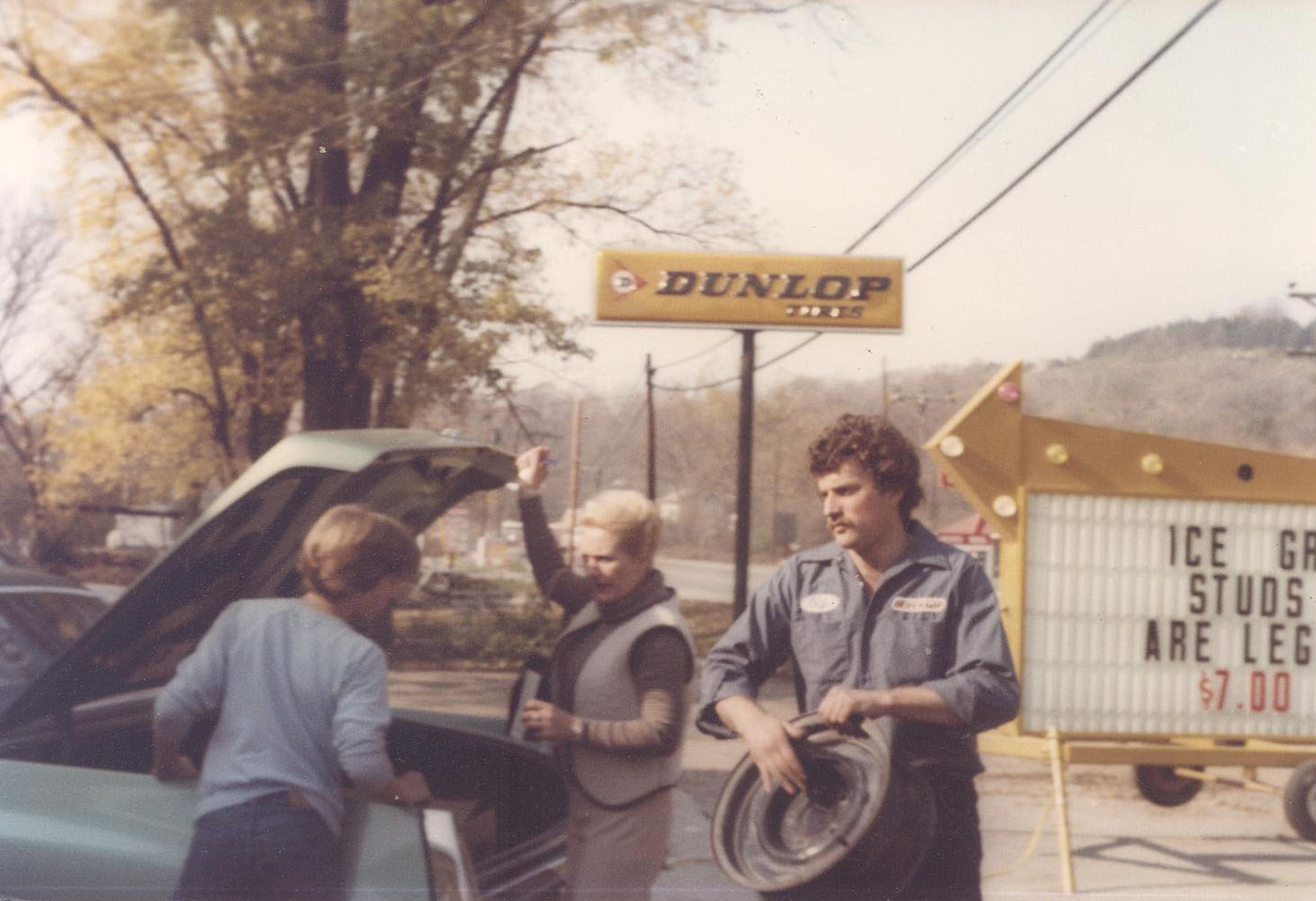 Three people working on a car with a Dunlop sign in the background